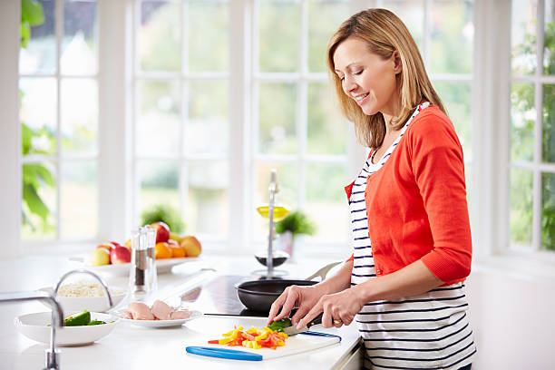 istock Women in cardigan cuts vegetables in white kitchen 460328379