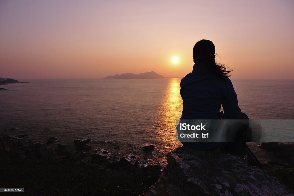 woman hiker sit on rock face the sunrise woman hiker sit on rock face the sunrise at seaside Mountain Stock Photo