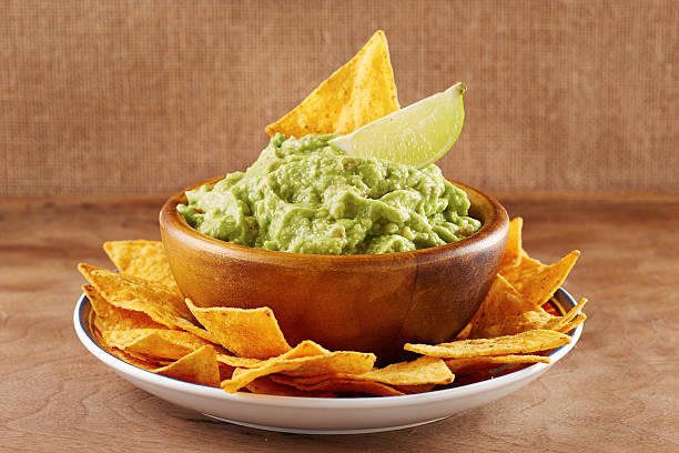 Mexican nacho chips with guacamole in a bowl and a lime Mexican nachos with handmade guacamole sauce on wooden table guacamole stock pictures, royalty-free photos & images