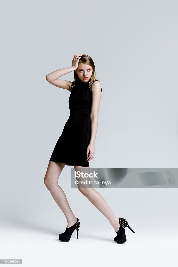 Beautiful slim woman Attractive young woman with perfect professional make-up and simple hairstyle, wearing beautiful black dress with gold spikes on the shoulders and high heels shoes. Fashion model full length body studio portrait on light background. 20-24 Years Stock Photo