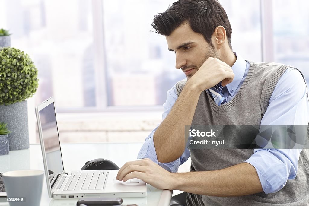 Young man with laptop Young man sitting at desk in office, working on laptop computer.. 20-29 Years Stock Photo