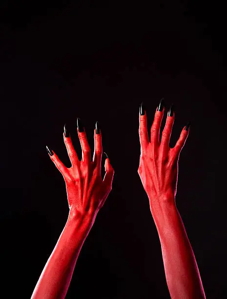 Red spooky devil hands with black nails, Halloween theme, studio shot on black background