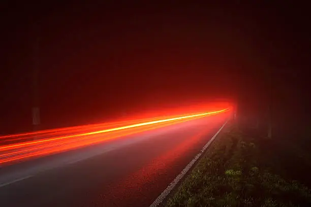 Nocturnal German country road in dense fog. Rear lights several cars shine through the fog. Federal Street in Brandenburg, Germany.
