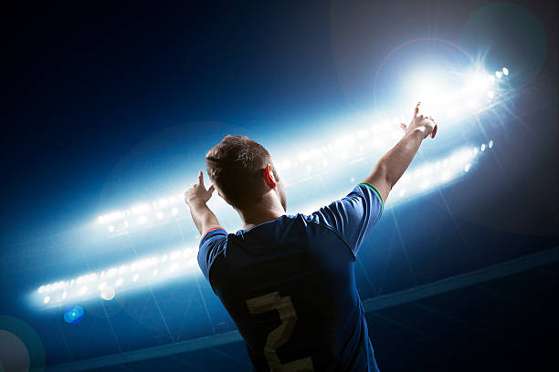 istock Soccer player with arms raised cheering, stadium at night time 460429653