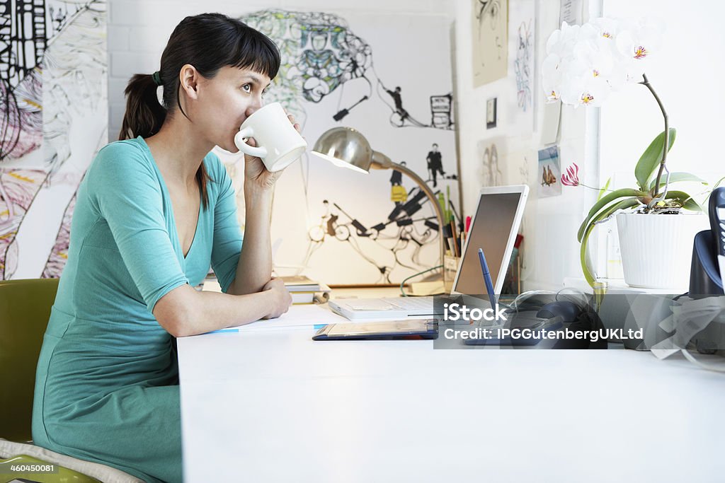 Businesswoman Drinking Coffee At Office Desk Side view of young businesswoman drinking coffee at office desk Adult Stock Photo