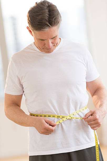 mann messen seinen taille im fitness-club - dieting front view vertical lifestyles stock-fotos und bilder