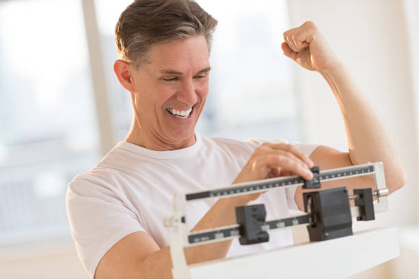 homem entusiasmado cerrar os punho enquanto a escala de peso - weight scale dieting weight loss imagens e fotografias de stock