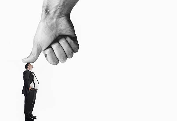 Businessman being pressed by thumb Businessman being pressed by thumb of giant hand, digital composite, colour enhanced, side view colour enhanced stock pictures, royalty-free photos & images