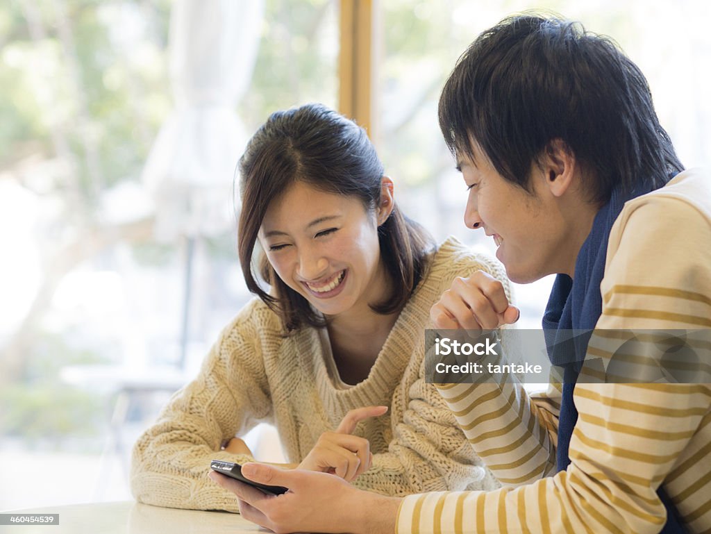 Young couple watching any contents on a smartphone A young couple watches any contents on a smartphone. A young man bas a smartphone on his hand. Japanese Ethnicity Stock Photo