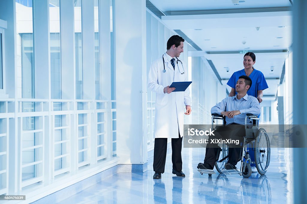 Man in wheelchair talking to his doctor and nurse Smiling female nurse pushing and assisting patient in a wheelchair in the hospital, talking to doctor Wheelchair Stock Photo