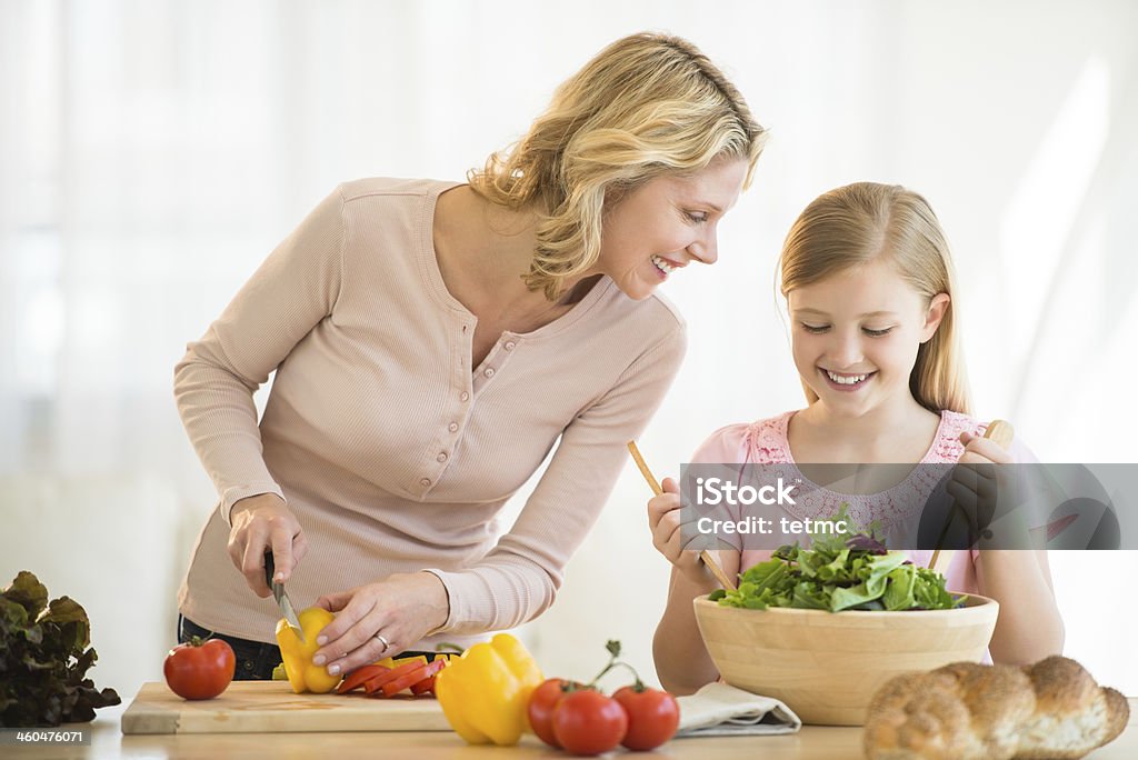 Girl Assisting Mother In Preparing Food At Counter Happy little girl assisting mother in preparing food at kitchen counter Cutting Board Stock Photo