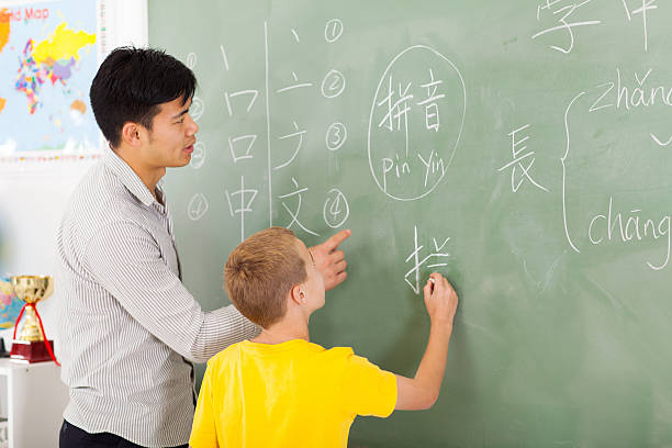 elementary school teacher helping young boy writing chinese friendly elementary school teacher helping young boy writing chinese on chalkboard chinese language stock pictures, royalty-free photos & images
