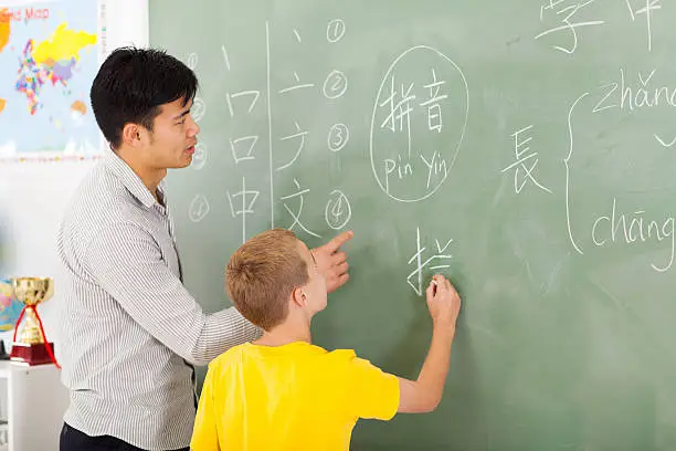 Photo of elementary school teacher helping young boy writing chinese