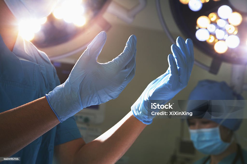 Midsection view of hands in surgical gloves and lights Midsection view of hands in surgical gloves and surgical lights in the operating room Surgery Stock Photo