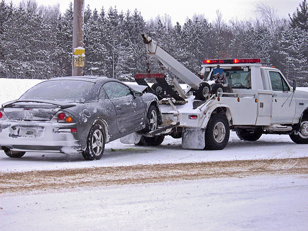 tow truck towing car Tow truck hauling a wrecked car away in winter. towing photos stock pictures, royalty-free photos & images