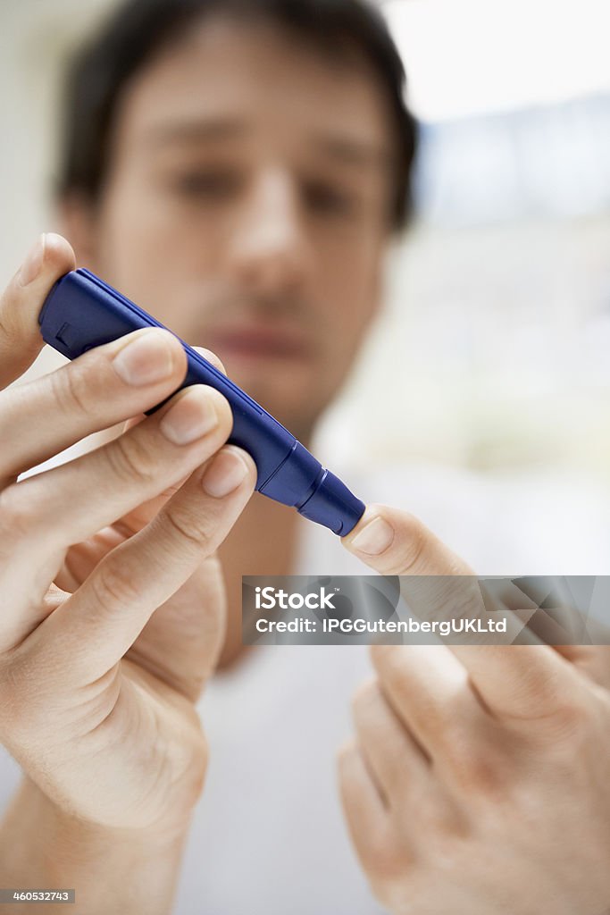Close-up of man's hands using a blue lancet on his finger Closeup of young man using lancelet on finger in bathroom Adult Stock Photo