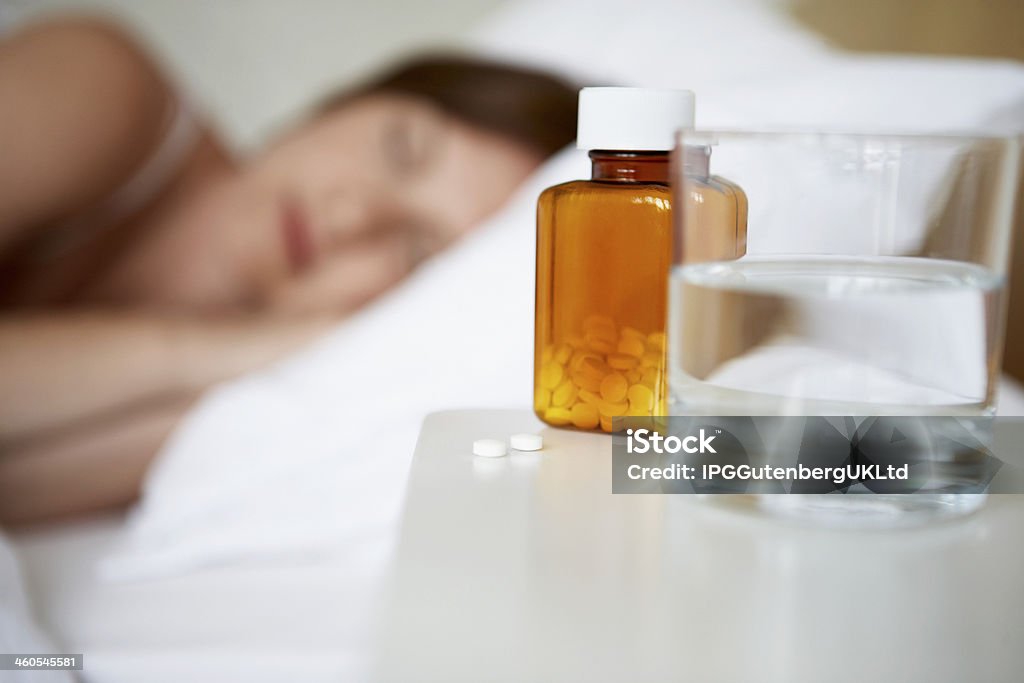 Sick mujer en la cama con pastillas en la mesa de noche. - Foto de stock de Adulto libre de derechos