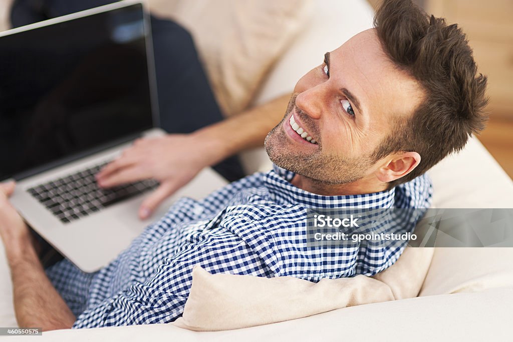 Smiling man using computer in living room Smiling man using computer in living room  Adult Stock Photo