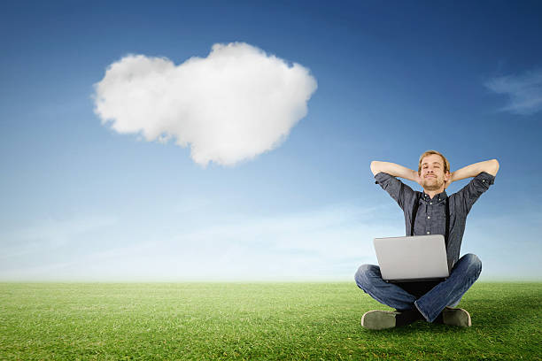 Man with laptop is relaxing on green meadow stock photo