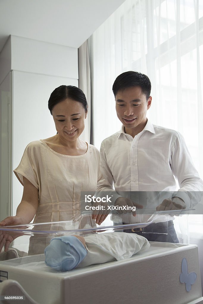 Young happy family looking down at their newborn Young happy family looking down at their newborn in the hospital nursery 35-39 Years Stock Photo