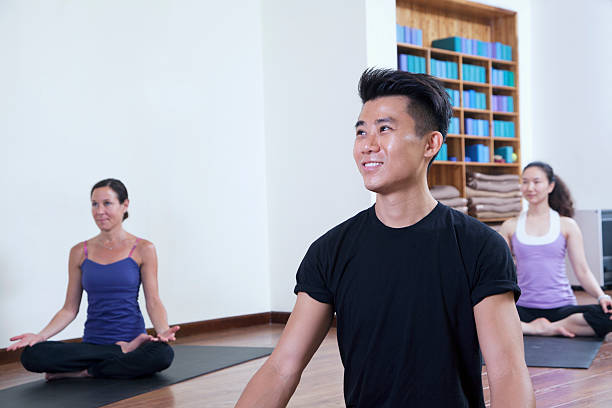 sorrindo homem sentado com as pernas cruzadas em uma aula de ioga - men yoga meditating cross legged - fotografias e filmes do acervo