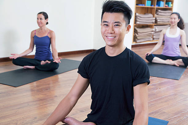 homme souriant assis assis en tailleur dans un cours de yoga - men yoga meditating cross legged photos et images de collection