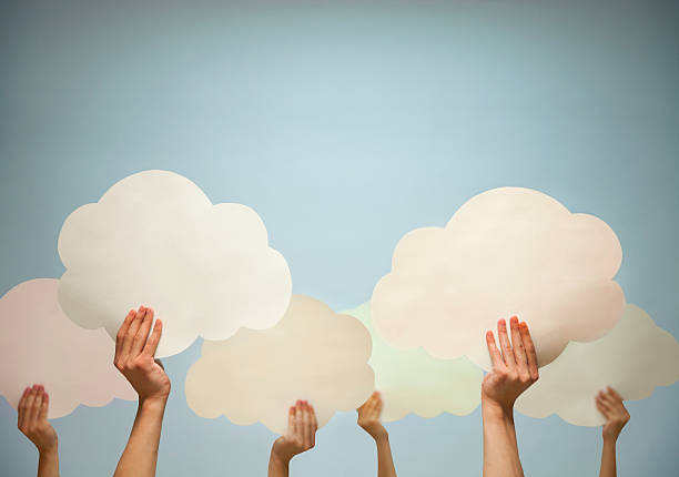 istock Multiple hands holding cut out paper clouds against blue background 460635873