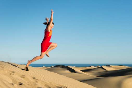 laughing girl jumping at sunset from sand dune with arms wide open - some motion blur   