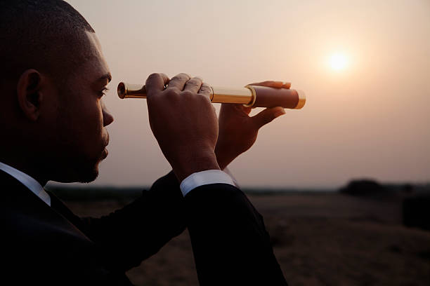 Businessman looking through spyglass in middle of the desert stock photo