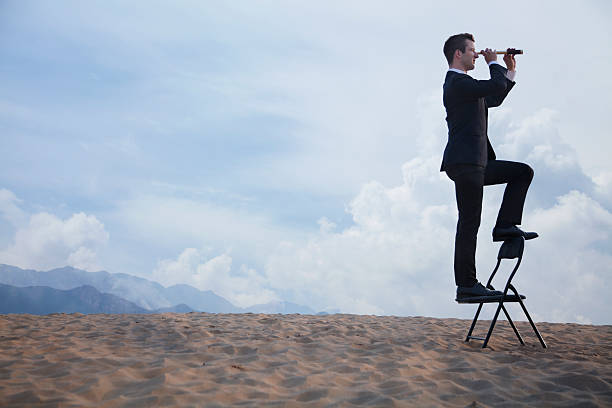 istock Businessman standing on a chair and looking through telescope 460648497