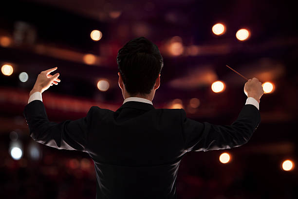 istock Young conductor with baton raised at a performance, rear view 460658061