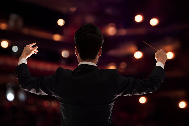 Young conductor with baton raised at a performance, rear view Young conductor with baton raised at a performance, rear view musical conductor photos stock pictures, royalty-free photos & images