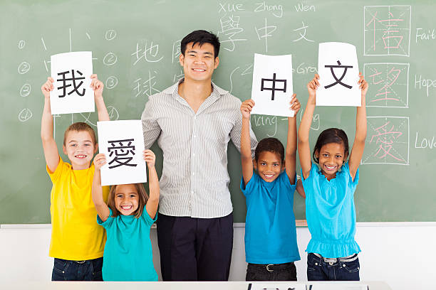 friendly male chinese teacher with group multiracial primary students holding papers saying i love chinese