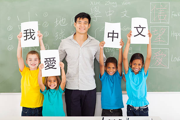 male chinese teacher with group multiracial students friendly male chinese teacher with group multiracial primary students holding papers saying i love chinese chinese language stock pictures, royalty-free photos & images
