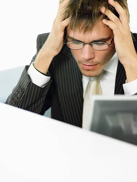 Stressed-out young businessman sitting at computer desk