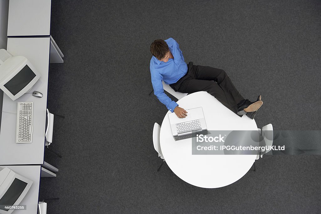 Businessman Using Laptop In Computer Room High angle view of relaxed businessman using laptop in computer room Accessibility Stock Photo