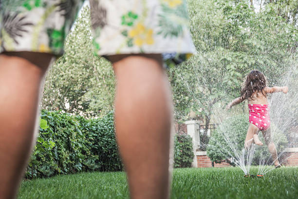 istock Little girl jumping through sprinkle as father watched, low section 460758157