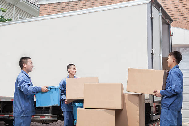 Movers standing by stack of cardboard boxes next to van stock photo