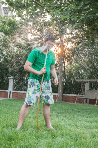 Young man spraying himself with a garden hose in the face, outdoors in the garden