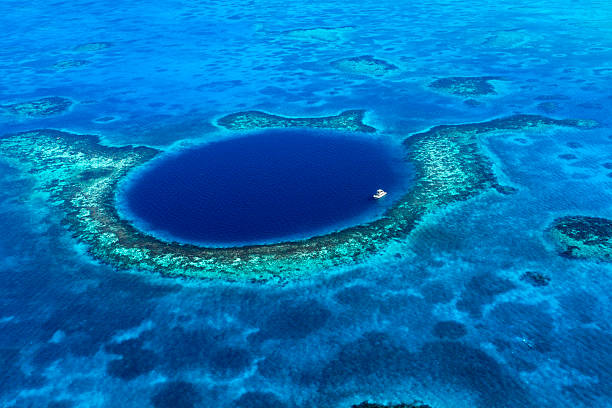 Great Blue Hole Belize An aerial view of a boat moored in the Great Blue Hole off the coast of Belize. The azure seas of the Caribbean envelope the deep blue of the Great Blue Hole. A coral reef surrounds the geologic wonder. atoll stock pictures, royalty-free photos & images