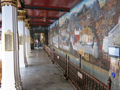 Bangkok, Thailand – December 16, 2013: Paintings on the wall inside Wat Pra Kaew. Tourists and locals inside Wat Pra Kaew or Temple of the Emerald Buddha, Bangkok, Thailand. Some walk around, and some take photos.  It is one of the main tourist attractions in Bangkok, and located in the historic center of Bangkok. It is located next to the Grand Palace.