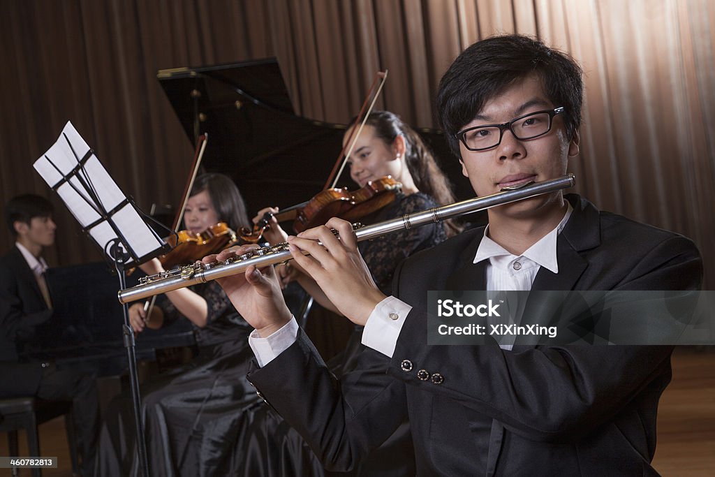 Flautist holding and playing the flute during a performance Flautist holding and playing the flute during a performance, looking at the camera Flautist Stock Photo