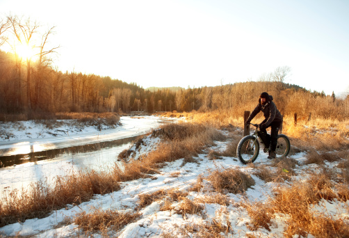 As the sun sets, a man is riding his snowbike on a trail alongside a river.