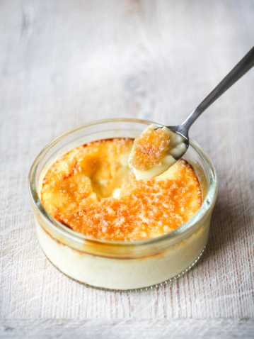 Crème Brulee in glass ramekin with spoon on light wooden table top