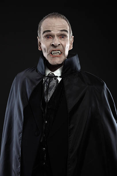 Dracula with black cape showing his scary teeth. Vamp fangs. Dracula with black cape showing his scary teeth. Vamp fangs. Studio shot against black. vampire stock pictures, royalty-free photos & images
