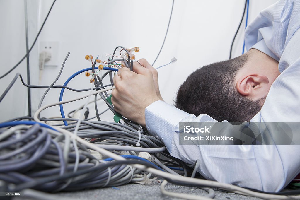 Frustrated man trying to figure out computer cables Frustrated man lying down trying to figure out and sort  computer cables Cable Stock Photo
