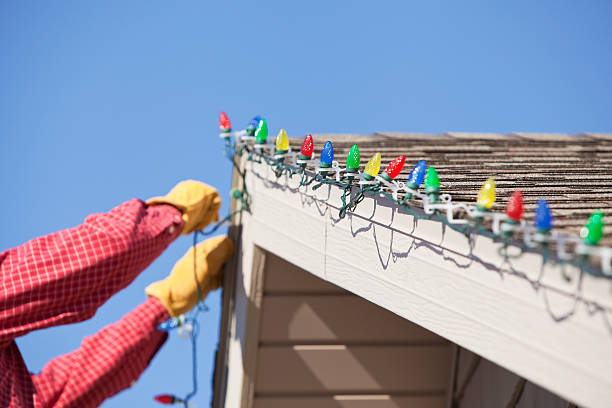Gloved Hands Installing LED Christmas Light on House Roof stock photo