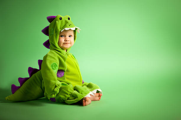 Baby Dinosaur A baby dressed as a green and purple dinosaur posing on a green background. carnival costume stock pictures, royalty-free photos & images