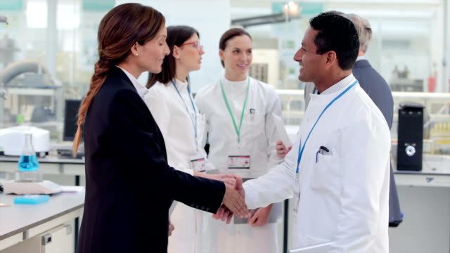 Businesswoman and scientist shaking hands in laboratory