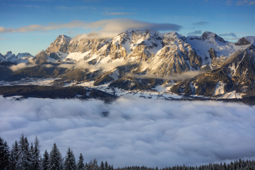 Beautiful Panorama of the famous Dachstein Glacier in the evening sun. The small village below is still covered in Fog while the last sun beams shape the impressive mountain.